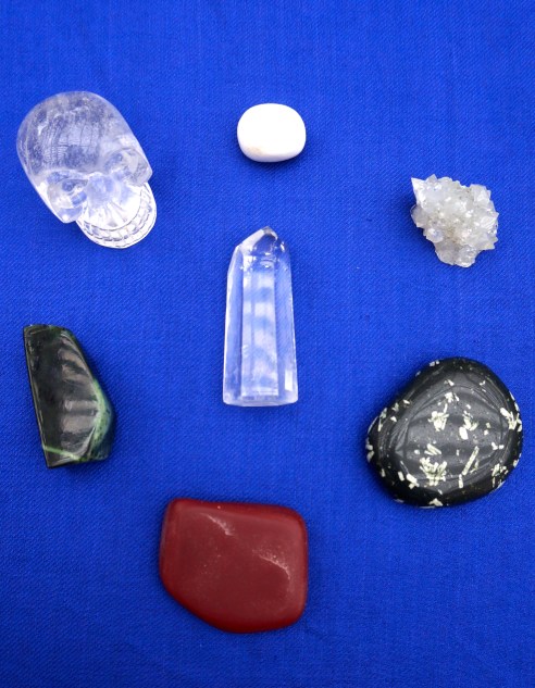 Clockwise from top: Scolecite, Apophyllite, Chinese Writing Rock, Pipestone, jade, quartz skull. Center: Quartz point. 
